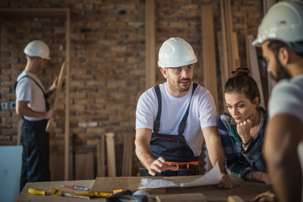 Manual workers and female architects talking while analyzing housing plan on construction site. EPLI Contractors Insurance