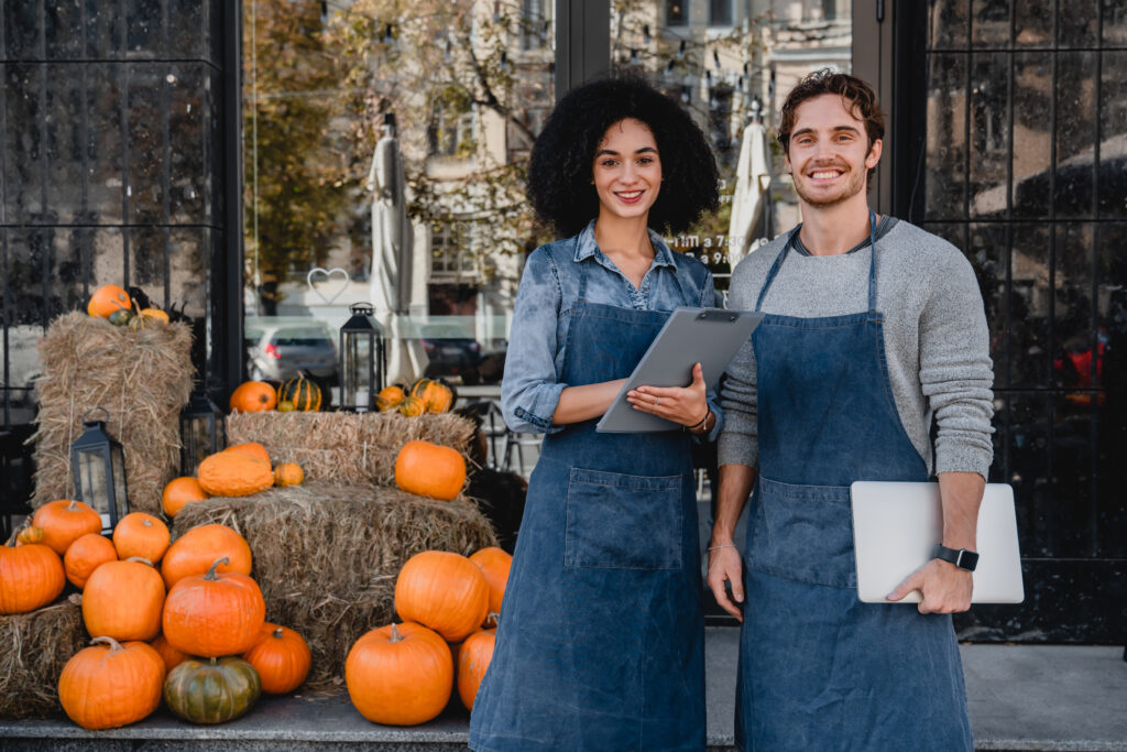 business owners stand outside store with pumpkins in background as they prepare business for halloween