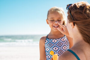Mother applies sunscreen to daughter's face at the beach
