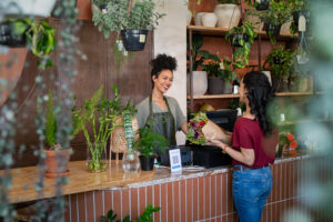 customer buys flowers from cashier at florist or flower shop, both smiling - business owner knows neighborhood, which is one way to help community prepare for hurricane!