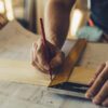 contractor using pencil to mark measurements on wood with ruler