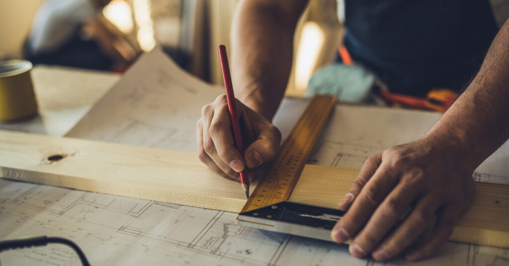 contractor using pencil to mark measurements on wood with ruler