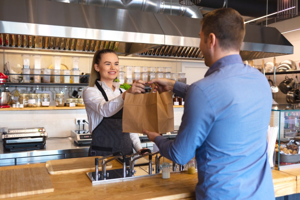 restaurant owner handing customer a bag of Super Bowl takeout food