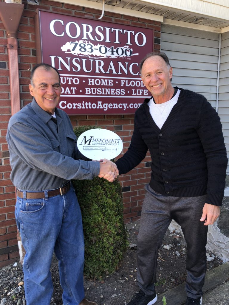 Policyholder and agent hold "Merchants Insurance Group" sign in front of Corsitto Insurance Agency