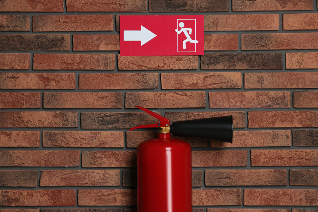 Fire extinguisher and emergency exit sign on brick wall indoors