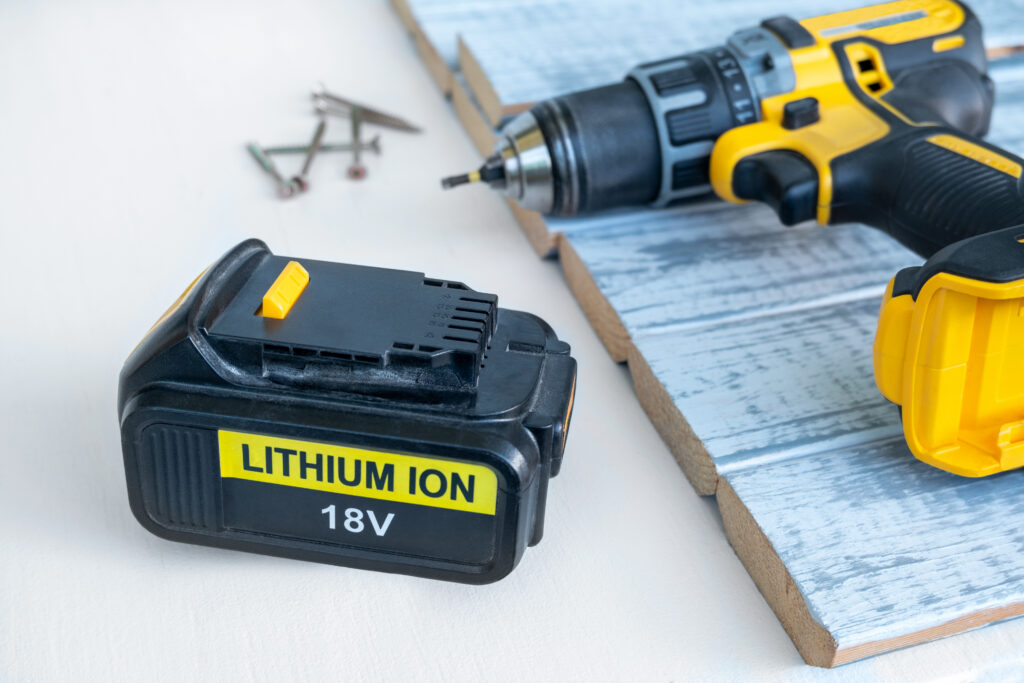 Close up 18 volt recharge Li-ion battery for electric cordless tool,saw,rotary hammer,drill,jigsaw,wrench on white.Blurred screwdriver,screws on gray-painted boards behind.